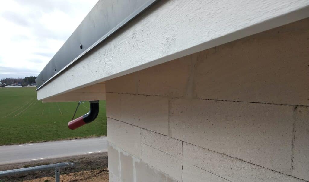 Building fasade under construction with unfinished wall and wooden roof boards with plastic gutter